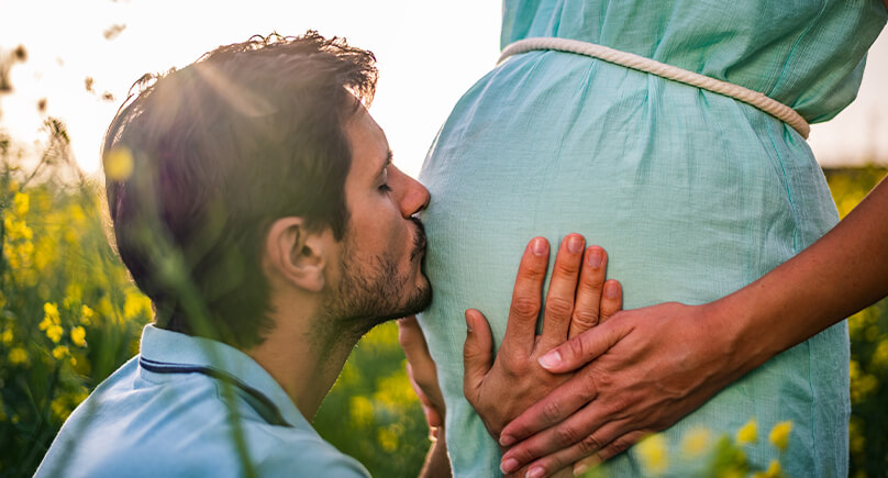 Junger Mann küsst den Bauch seiner schwangeren Partnerin