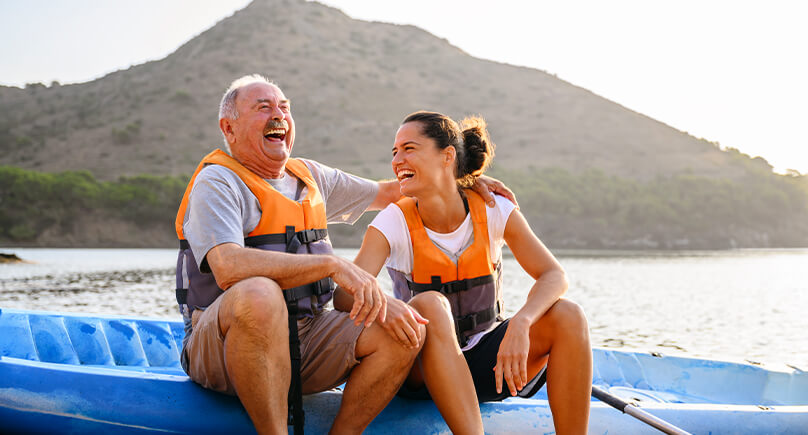 Senior und eine Frau sitzen mit Rettungswesten auf einem Boot und lachen